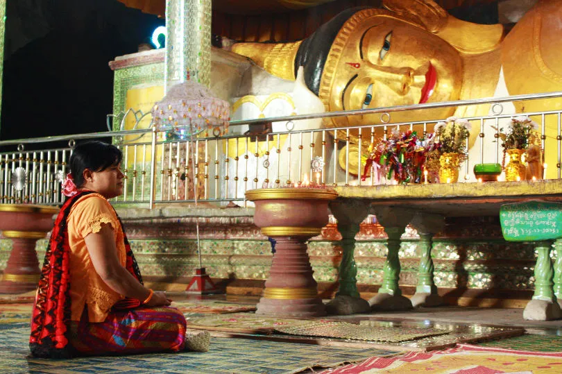 Eine Frau kniet vor einem Buddha in Myanmar