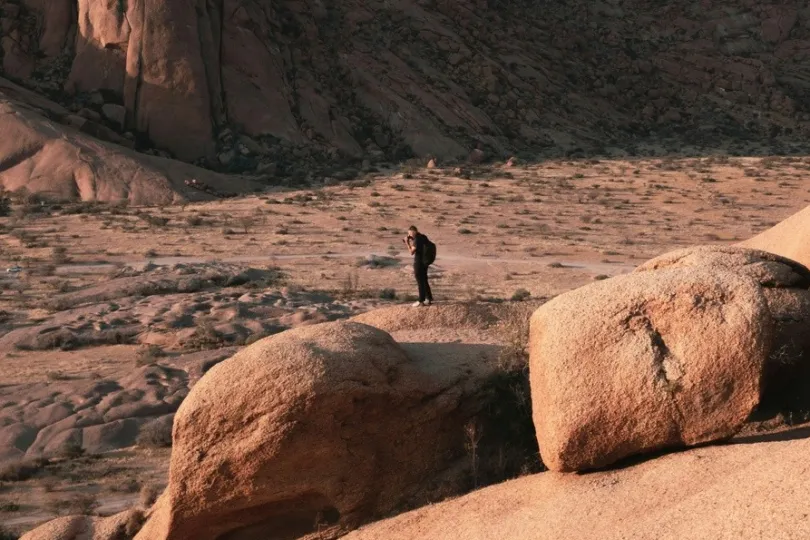 eine Person steht in einer felsigen Wüstenlandschaft und macht bilder mit sein Kamera.
