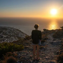 Eine Frau steht an einer Klippe in Griechenland und schaut auf das Meer