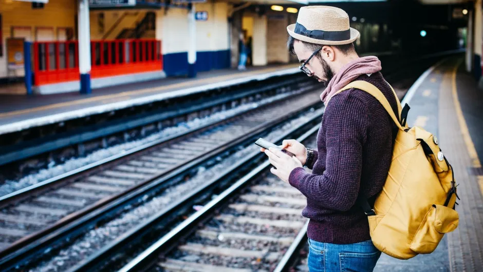 Ein Reisender steht am Bahnhof und prüft seine Reise App
